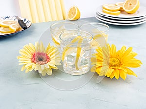 Lemon water drink with ice cubes on stone background with gerbera daisy yellow flowers