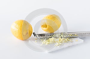 Lemon zest with a microplane and two lemons in behind.