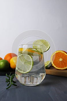 lemonade citrus orange lime lemon in a glass with ice and rosemary on a gray background next to the fruits close-up. Preparation