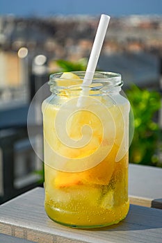 Lemonade cocktail with lemon in glass jar, cold refreshing drink or beverage with ice at a rooftop bar.