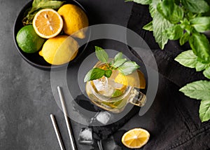 Lemonade drink with fresh lemon, lime, mint and ice in a jar. Refreshing citrus mojito cocktail or cold tea on a dark background.