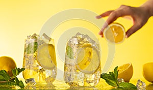 Lemonade with fresh slice lemon and mint leaves. Woman holding half of lemon. Summer homemade drink