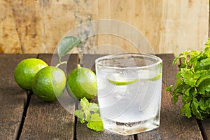 Lemonade in glass and green lemon on wooden background.Drink for health.Close up