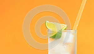 Lemonade with ice and lime on a bright orange background