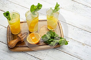 Lemonade with orange and mint, cold refreshing drink in glasses on white wooden background