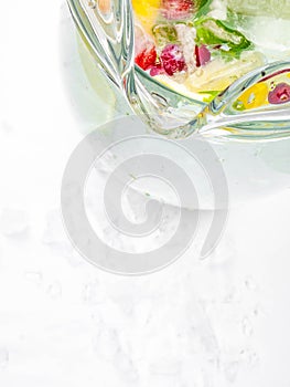 Lemonade pitcher with lemon slices, mint leaves, red berries and ice cubes, glass jug. View with copy space