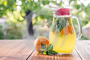 Lemonade pitcher with orange, mint and ice on garden table. Homemade orange lemonade with mint