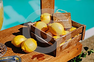 Lemonade table with a box of lemons, silver trays and decanters of lemonade on the edge of the pool with a turquoise water