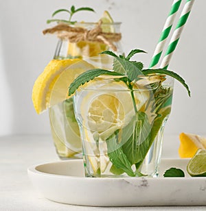 Lemonade in a transparent glass with lemon, lime, rosemary sprigs and mint leaves on a white background