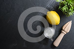 Lemons with juice squeezer and glass of lemon juice are on top of black stone table. Top view with copy space, flat lay. Low key