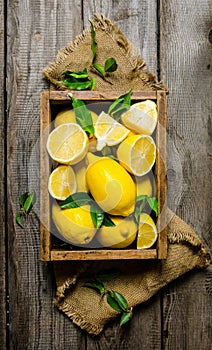 Lemons with leaves in a box on the fabric. On wooden background.