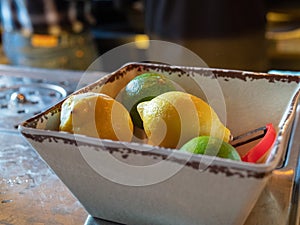 Lemons and limes with peeler sitting in bowl of a bar for bartenders to make cocktails