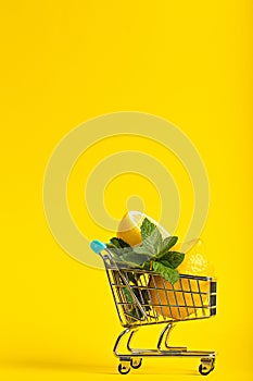 Lemons and mint in a small toy cart on a banana yellow background. online shop delivery concept