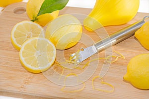 Lemons, squeezer, zest and Zester on wooden cutting board.