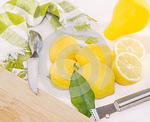 Lemons, squeezer, Zester, knife and wooden cutting board.