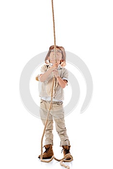 Length view of explorer kid in hat and glasses holding rope and looking up on white