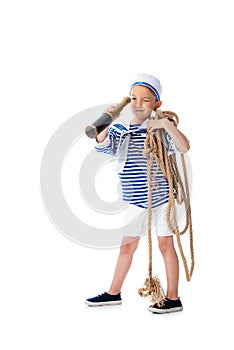 Length view of focused preschooler child in sailor costume looking in spyglass and holding rope isolated on white