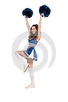 Length view of happy cheerleader girl in blue uniform dancing with pompoms isolated on white