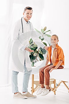 Length view of smiling pediatrist in white coat and child in clinic