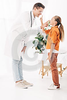 Length view of smiling pediatrist in white coat and child in clinic