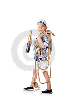 Length view of smiling preschooler child in sailor costume holding spyglass and rope on white