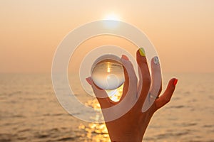 Lens ball in hand with reflection of sea and sunset on the beach