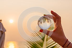 Lens ball in hand with reflection of sea and sunset on the beach