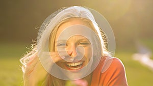 LENS FLARE: Beautiful young woman lying in a meadow and laughing to a joke.