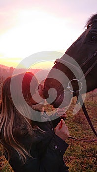 LENS FLARE: Caring young woman kisses her beautiful brown horse on the muzzle