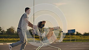 Lens flare: Cheerful people couple man and woman at sunset ride supermarket trolleys in slow motion