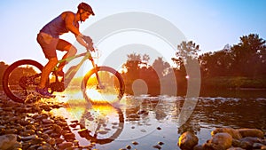 LENS FLARE: Cinematic shot of mountain biker riding across a river at sunset.