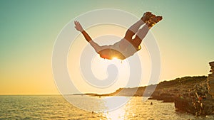 CLOSE UP: Beautiful golden sunbeams shine on fit man cliff diving at sunset.