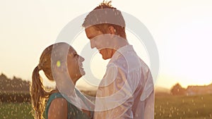 LENS FLARE: Easygoing couple laughs while they dance in nature on rainy evening.