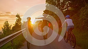 LENS FLARE: Group of cyclists rides ebikes along empty country road at sunset.