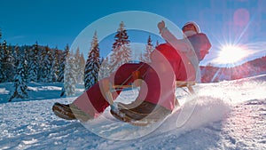 LENS FLARE: Joyful woman sleds down snowy hill in the sunny Slovenian mountains.