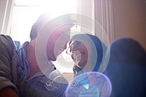 Lens flare, relax or happy couple laughing in home living room in conversation and speaking together. Man, funny woman