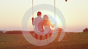 LENS FLARE SILHOUETTE Young couple swaying on swing,gazing into crimson sunset