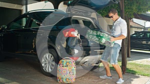 LENS FLARE: Smiling man in white shirt unpacking luggage from large black car.