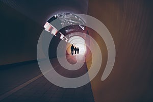 Lens-flared silhouettes of people in a circular tunnel for pedestrians and cyclists.