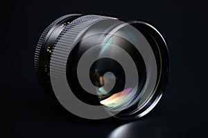 The lens of a SLR or mirrorless camera with colored highlights on the front lens on a black background