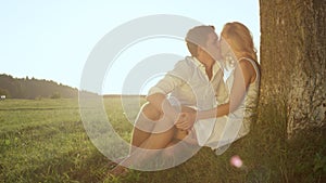 LENSE FLARE: Loving young couple sharing a kiss under a tree in sunlit meadow