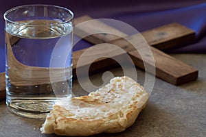 Lent season concept. Water, bread and cross on background of violet fabric