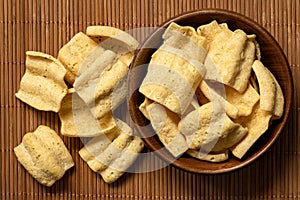 Lentil chips in a rustic wood bowl next to a pile of lentil chips on bamboo matt from above