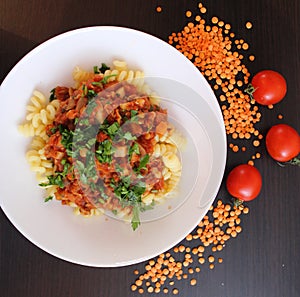 Lentil pasta with tomato sauce, parsley in a white plate on a dark table. Lentil beans on the side and cherry tomatoes