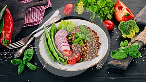 Lentil with radish, cherry tomatoes, beans and vegetables. Healthy food. On a black wooden table.