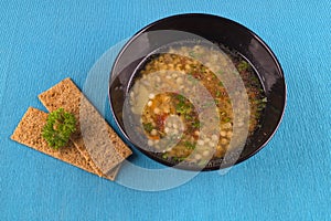 Lentil soup with herbs in black mask on a blue background.