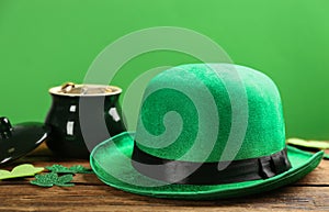 Leprechaun hat, decorative clover leaves and pot of gold on wooden table against green background. St Patrick`s Day celebration