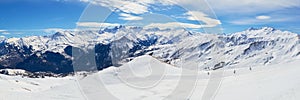 Les Sybelles ski domain in France. Panorama with slopes, skiers, and mountain peaks, on a sunny day with blue sky