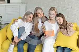 Lesbian couple in casual clothes with their daughters reading a book