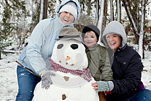 A lesbian couple with a child posing with a snowman in a forest.